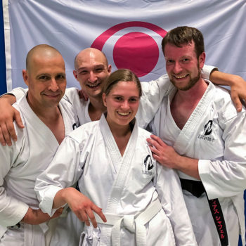 Vier Personen in Karate Anzügen vor der Flagge der Insel Okinawa.