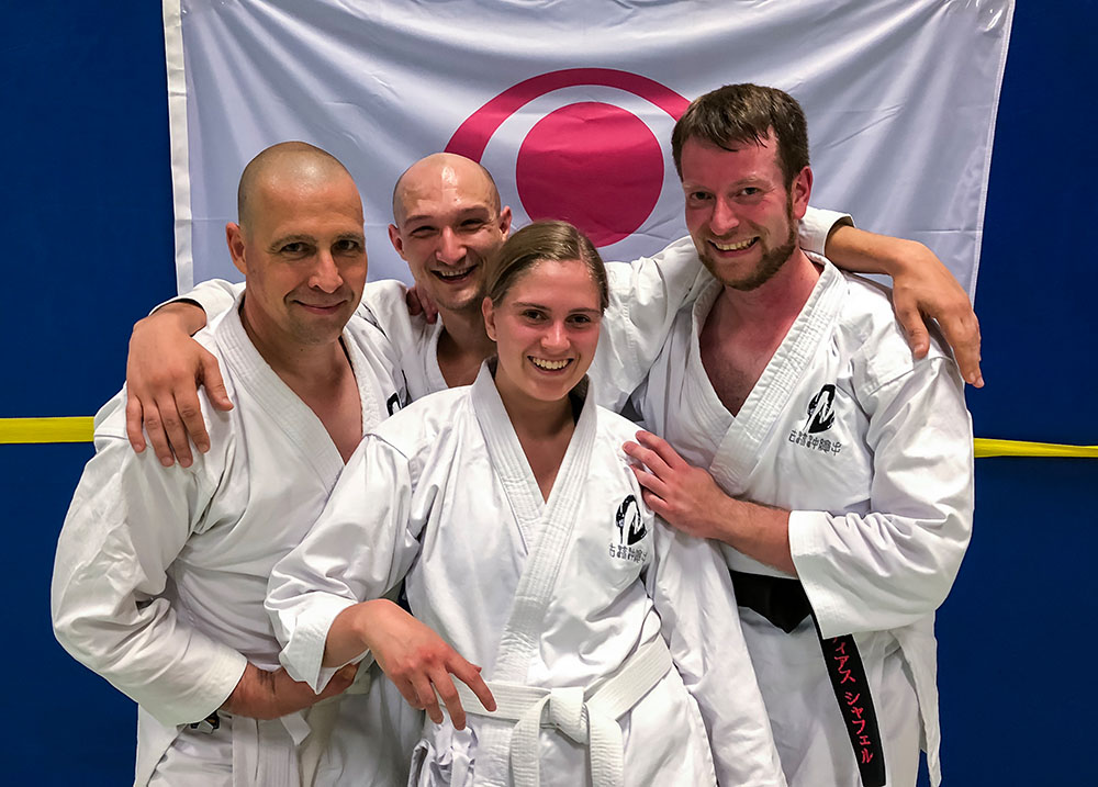 Vier Personen in Karate Anzügen vor der Flagge der Insel Okinawa.